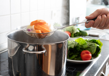 A Person ladles vegetabels into a large stock pot