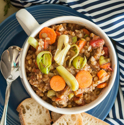 Bowl of Lentil vegetable soup with bread on a table with carrots and tomatoes.