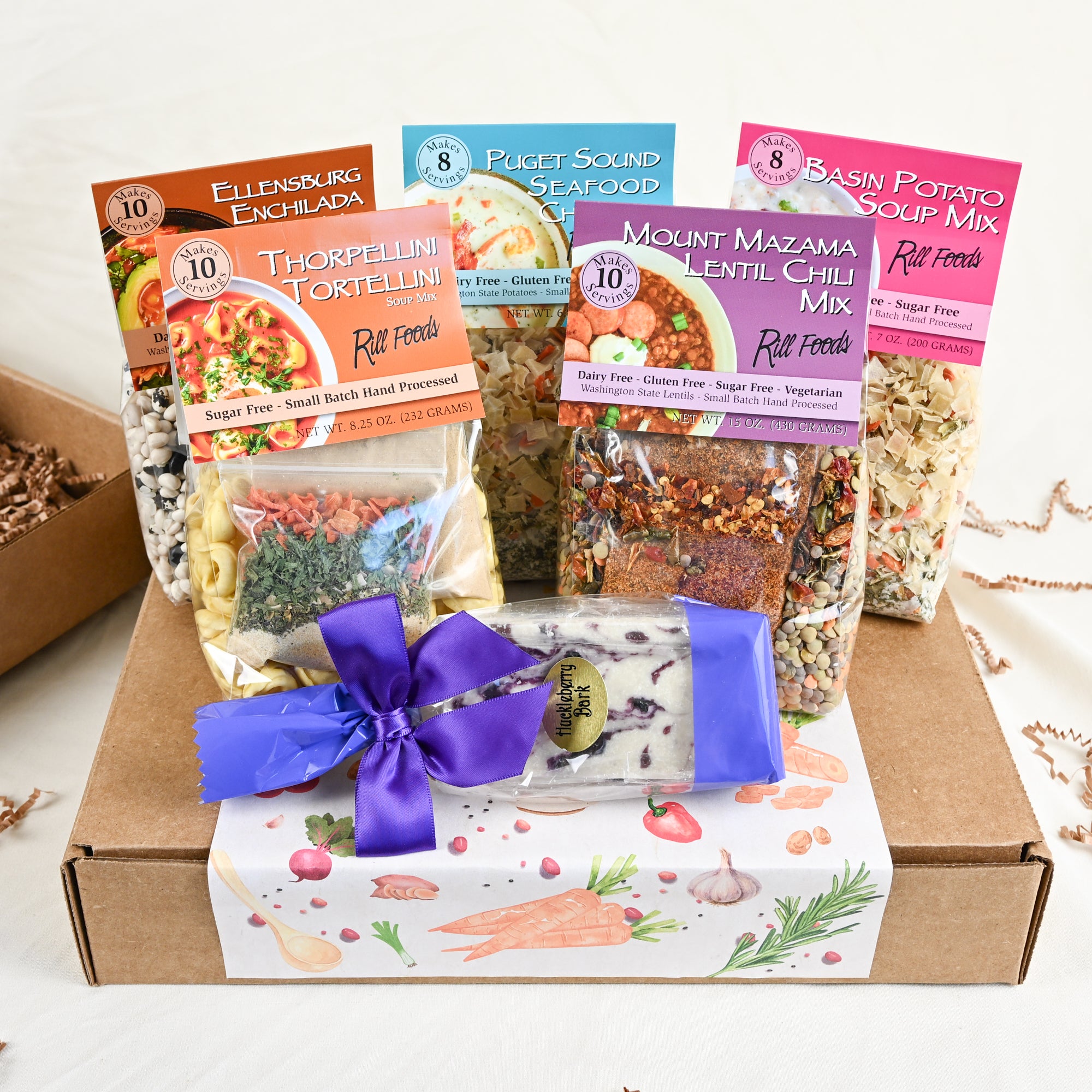 Assorted food packages on top of a gift box including pasta, soup mix, and a purple ribbon on a white background
