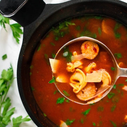Spoonful of pasta soup with tomatoes and herbs on a white background