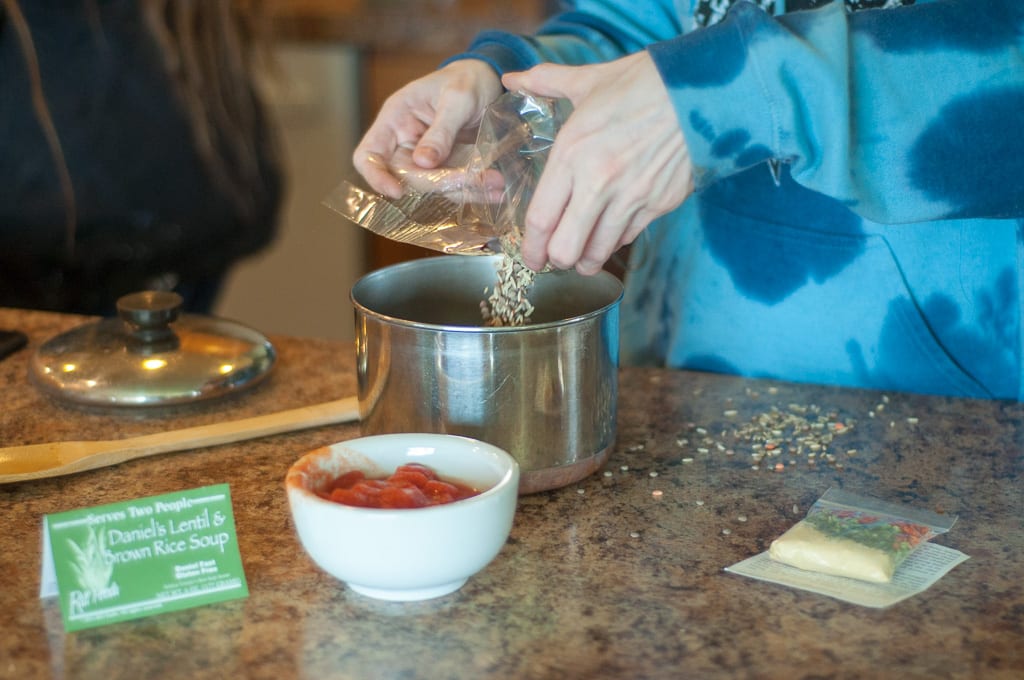 pictured is someone adding the Daniel's Lentil and Brown Rice Soup mix to a sauce pan to prepare it