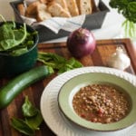 A bowl of lentil soup next to some fresh ingredients