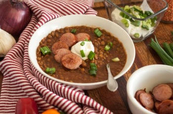 This image shows lentil soup with toppings such as sour cream, cooked sausage, and green onions.